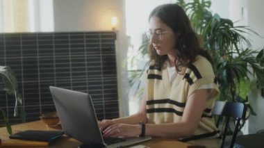 Bilgisayarda çalışan genç bir kadın ofis masasında güneş paneli ve yeşil bitkilerle çalışıyor.