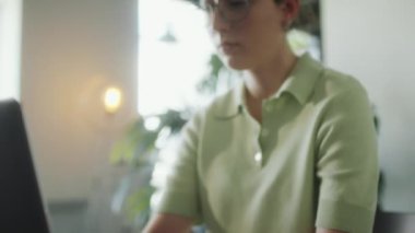 Gözlüklü ve sıradan tişörtlü bir kızın evde çalışırken ya da internette çalışırken bilgisayarını kullanırken yakın plan fotoğrafını çek.