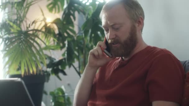 Mladý Vousatý Muž Sedí Doma Pohovce Mluví Telefonu Používá Notebook — Stock video