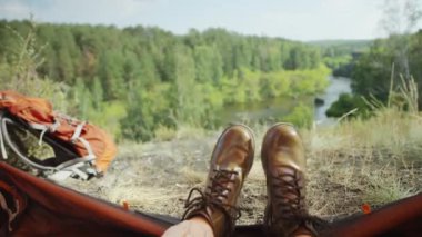 Kamp alanında çadırda oturan ve güzel nehir ve yeşil ormanı seyreden çizmeli kadın turist.