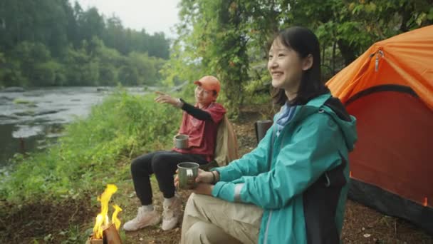 Duas Turistas Asiáticas Sentadas Lado Fogueira Margem Rio Bebendo Chá — Vídeo de Stock