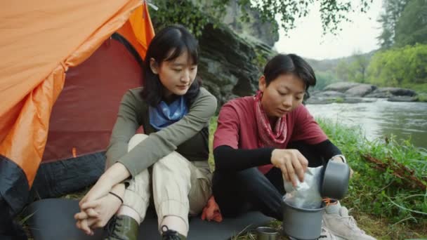 亚洲女游客在河岸的营地准备食物时 把铝箔袋放在便携式煤气灶的锅里 — 图库视频影像