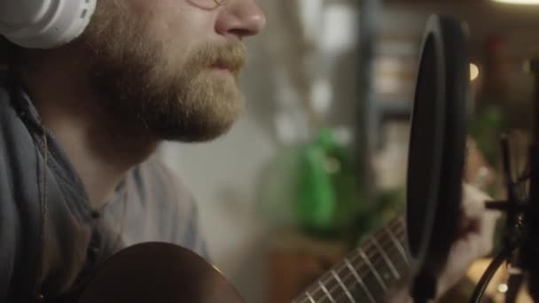 在家里的音乐工作室里 用耳机拍下了男人弹吉他和用麦克风唱歌的特写 — 图库视频影像