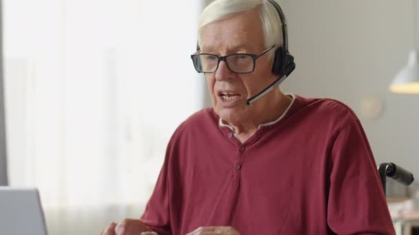 家で車椅子に座ってノートパソコンでビデオ通話で話している高齢者のショットを下に傾ける — ストック動画