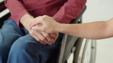 Tanımlanamayan bir kadının, tekerlekli sandalyedeki yaşlı bir adama destek olurken elini sürdüğü kesme sahnesi.