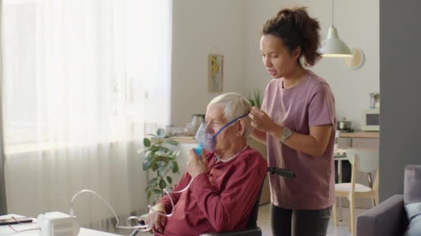 Θηλυκός Φροντιστής Που Βοηθά Ηλικιωμένο Άνδρα Αναπηρική Καρέκλα Χρησιμοποιήσει Νεφελοποιητή — Αρχείο Βίντεο