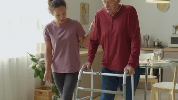 女性介護者は 老人が家での日常生活活動を支援しながら歩行者を利用するのを助ける — ストック動画