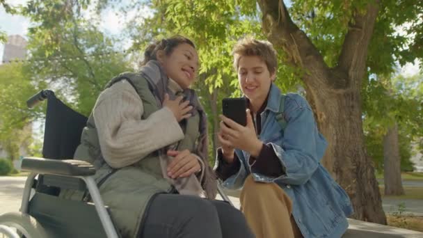 Glückliche Junge Frau Rollstuhl Lächelt Und Winkt Mit Der Smartphone — Stockvideo