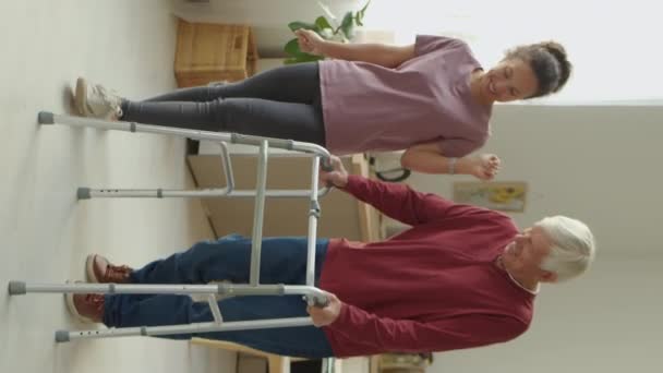 垂直フルショットの陽気な女性介護者とチャットシニア男として彼使用ウォーカー一緒に家の周りを歩く — ストック動画