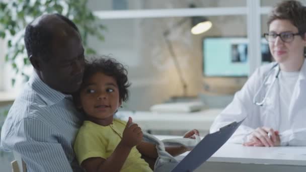 African American Dad Sitting Little Son Clinic Reading Medical Agreement — Stok video