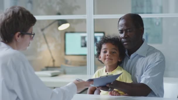 非裔美国人父亲与小儿子坐在一起 为医生提供病历 并在儿科诊所的咨询期间发言 — 图库视频影像