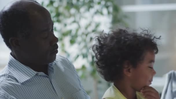 かわいいアフリカ系アメリカ人の少年が父親と座り 女性医師が小児診療所で診察中に懐中電灯を点検 — ストック動画