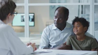 African American father and little son speaking with female pediatrician on consultation in clinic