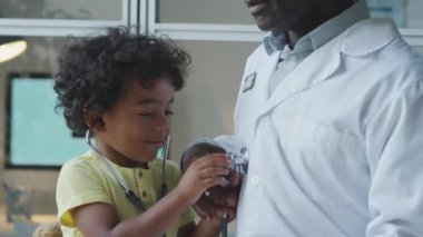 Küçük Afrikalı Amerikalı çocuk steteskopla oynuyor ve pediatri kliniğinde erkek doktoru muayene ediyor.