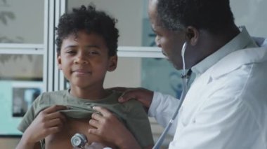 Klinikteki sağlık kontrolü sırasında küçük çocuğu muayene ederken steteskop kullanan Afrikalı Amerikalı bir çocuk doktoru.