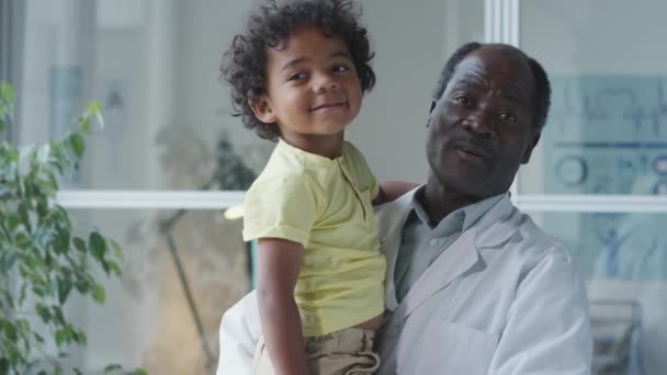 Portrait Happy African American Pediatrician Holding Cute Little Boy Arms — Αρχείο Βίντεο