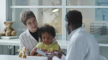 Çok ırklı anne ve küçük oğlu kliniği ziyaret ederken Afrikalı Amerikalı çocuk doktoruyla konuşuyor.