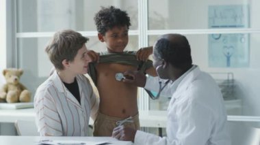 Klinikteki çocuk doktorundan sağlık kontrolü aldıktan sonra annesine sarılan Afrikalı Amerikalı çocuk.