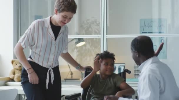 African American Pediatrician Greeting Little Boy Wheelchair Hand Clasp Talking — Stockvideo