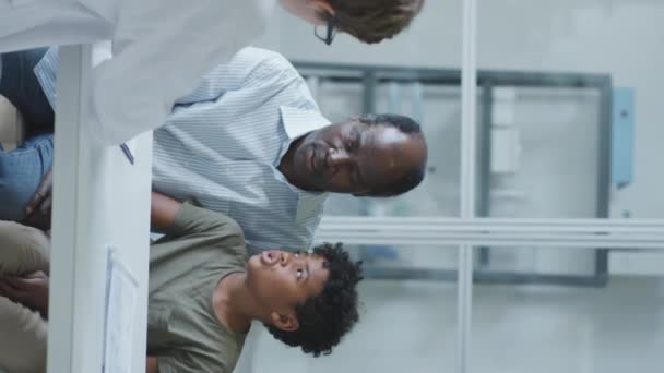 Вертикальный Снимок Афроамериканца Сидящего Маленьким Сыном Педиатрической Клинике Беседующего Женщиной — стоковое видео
