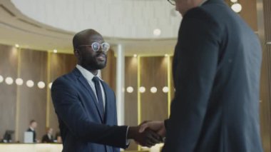 Afrikalı Amerikalı iş adamının otel lobisinde beyaz meslektaşını selamlarken orta boy bir fotoğraf.