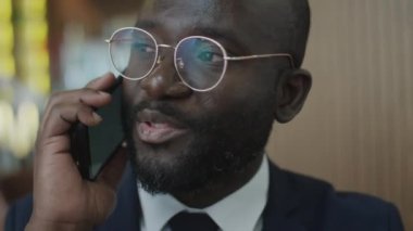 Restoranda gözlüklü Afrikalı Amerikalı işadamının cep telefonuyla konuşurken yakın plan fotoğrafı.