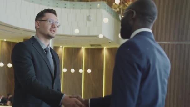 ホテルのロビーでアフリカ系アメリカ人とコーカサス人のビジネスマンミーティングのメディアショット 握手と話す — ストック動画