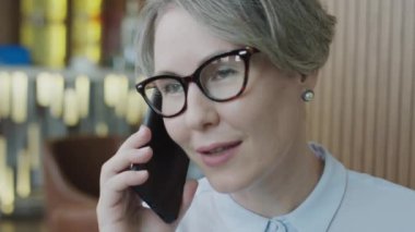 Kafkasyalı iş kadını gözlüklü ve resmi tişörtlü restoranda telefonda konuşurken yakın çekim.