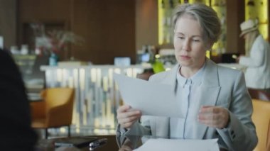 İş kadını sözleşmeyi okuyor, kağıtları imzalıyor ve restoran toplantısında ortağına tokalaşıyor.