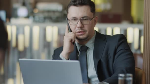 Наклоните Снимок Бизнесмена Сидящего Столом Ресторана Ноутбуком Разговаривающего Мобильному Телефону — стоковое видео