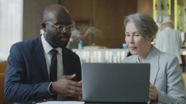 Afro-Amerikalı işadamı ve Kafkasyalı iş kadını birlikte restoran masasında oturmuş laptopta bir şeyler tartışıyorlar.