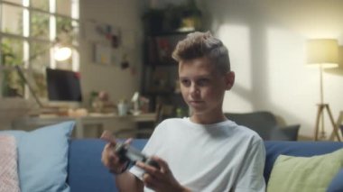Evdeki kanepede oturup konsol oyunu oynayan heyecanlı gencin orta boy fotoğrafı.