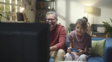 Genç kız babasıyla evde video oyunu oynuyor, ellerini kaldırıyor ve zaferi kutluyor.
