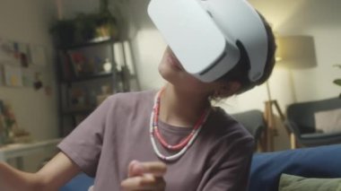 VR kulaklıklı genç kız evde sanal gerçeklik oyunu oynarken sağa sola hareket ediyor