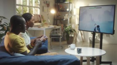 Afro-Amerikalı çift oturma odasında kanepede oturuyor ve TV 'de video oyunu oynuyorlar.