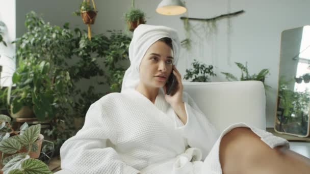 가운과 식물로 꾸며진 방에서 의자에서 전화에 수건에 머리에 여자의 샷에서 — 비디오