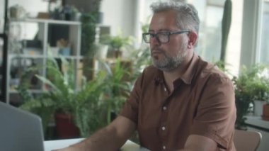 Orta yaşlı iş adamının rahat ofisteki dizüstü bilgisayarda çalışırken çekimini kaldır. Bitkilerle süslenmiş.