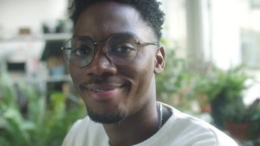 Gözlüklü genç Afro-Amerikan bir adamın yakın portresi ofiste gülümseyerek kameraya poz veriyor.
