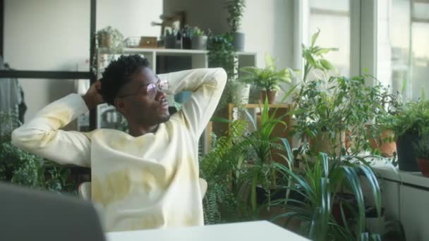 在办公室休息期间 穿着休闲装 双手放在脑后 装饰着室内植物的非洲裔美国年轻人的中景照片 — 图库视频影像