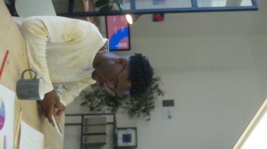 Genç siyahi adamın iş yerinde otururken cep telefonuyla mesajlaşırken dikey görüntüsü.