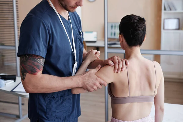 Massagist in uniform examining body of patient before massage procedure in hospital