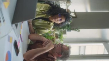 Genç Latin kadın ve orta yaşlı beyaz adamın laptopta iş projesini tartışırken çekilmiş dikey bir fotoğrafı.