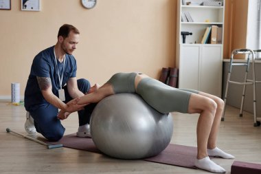 Hastanede rehabilitasyon sırasında fitness topu eğitimi alan bir terapist.