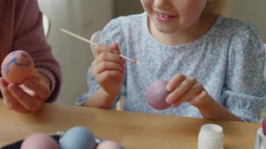Mutlu anne ve küçük kızın paskalya yumurtalarını boyarken ve evde tatile hazırlanırken gülümserken yakın plan çekimleri.