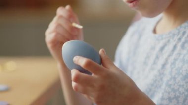 Küçük bir kızın boyalı Paskalya yumurtasını boya ve fırçayla süslemesi.