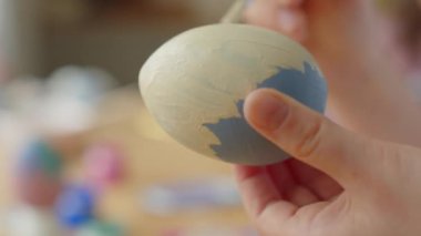 Paskalya yumurtasını süslemek için boya fırçası kullanan çocuğun ellerini yakın plan çek.