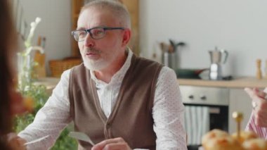 Büyükbaba, tatilde evde yemek yiyor ve aile üyeleriyle konuşuyor.