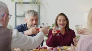 Aile çifti ve onların kıdemli aileleri kadeh tokuşturuyor, yemek masasında sohbet ediyor ve gülümsüyor evde birlikte Paskalya kutlarken.