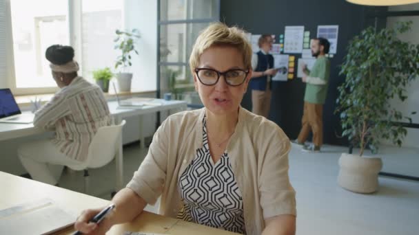オフィス勤務中のオンラインビデオ通話でビジネスプランを議論しながら 紙やカメラで財務グラフを表示する女性 — ストック動画