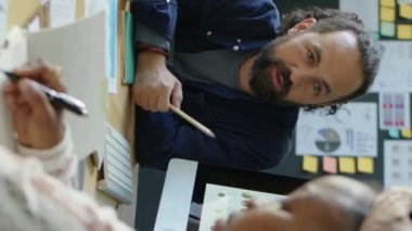 İş adamının ofiste iş arkadaşlarıyla bilgisayar ekranında finansal bilgileri tartışırken dikey görüntüsü